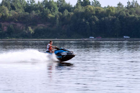 Riga, Salaspils, Latvia, 08.30.2018: a white, Caucasian attractive man on a blue water motorcycle, in the background the shore with a growing forest and several carsのeditorial素材