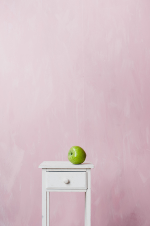 A green apple lies on a white vintage pedestal on a pink background.の写真素材