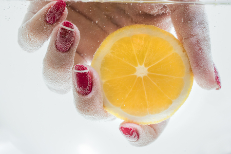 Female hand holding a slice of fresh lemon under water.の写真素材