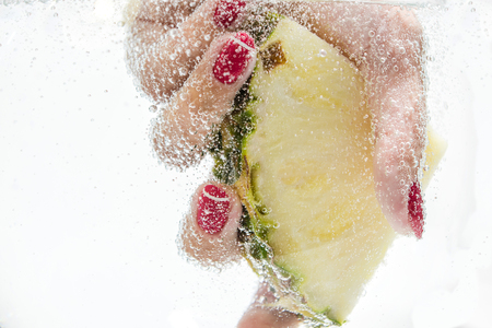 Female hand holding a slice of fresh pineapple under water.の写真素材