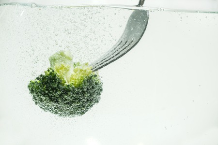 Pieces of fresh appetizing broccoli on a fork in clear water. Close-up photo.の写真素材