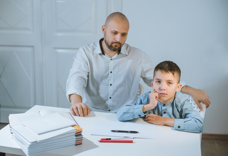 Sad kid sitting at a table next to his father, who is angry at him.の写真素材