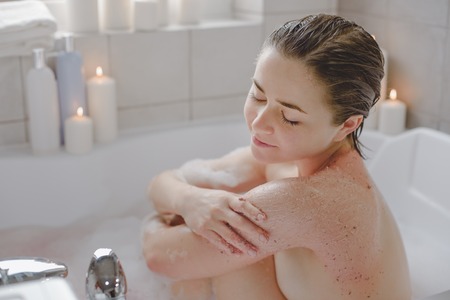 A young beautiful woman uses a body srab in a bath.の写真素材