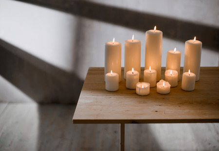 A group of different sized candles stands on a simple wooden table.の写真素材