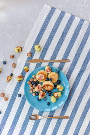Fresh cheese pancake, ripe figs, jujube, blueberry and raw hazelnuts on a blue plate.の写真素材