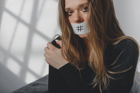 Portrait of a young beautiful sad girl, whose mouth is sealed with a hashtag.の写真素材