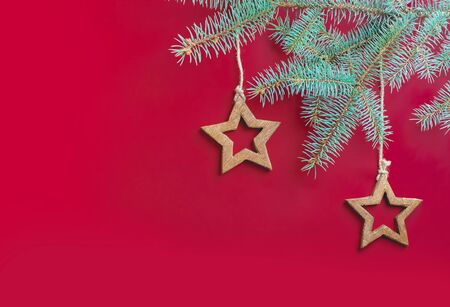 Golden wooden stars hung on a spruce branch on jute ropes on a red background. Christmas photo.の写真素材