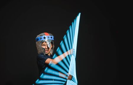 A kid with a light saber in his hands play in a superhero battle.