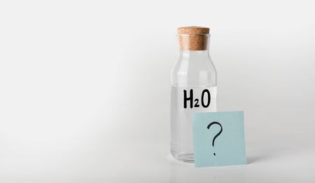 Glass bottle with the inscription chemical formula of water on it and a white transparent liquid...