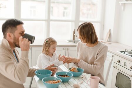 Young cute family with little daughter have breakfast at home in the kitchen.の写真素材