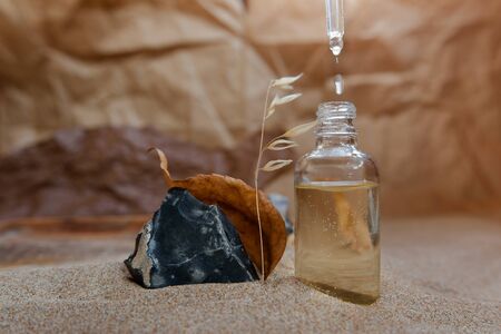 Bottle with a pipette, filled with essence, oil or perfume. Background sand and craft paper.