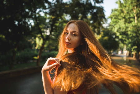 Young beautiful red-haired long-haired woman in a summer pink dress walks through the streets of a...
