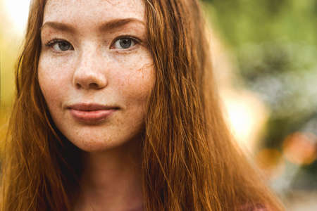 Young beautiful red-haired long-haired woman in a summer pink dress walks through the streets of a summer city.の写真素材