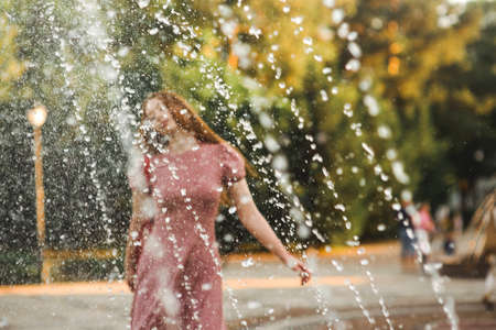 Young beautiful red-haired long-haired woman in a summer pink dress walks through the streets of a...