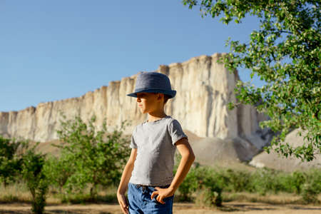 A cheerful kid in jeans, a T-shirt and a blue hat is playing in the garden among the apple trees.の写真素材