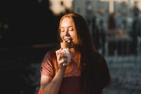 Young beautiful red-haired long-haired woman in a summer pink dress walks through the streets of a summer city.の写真素材