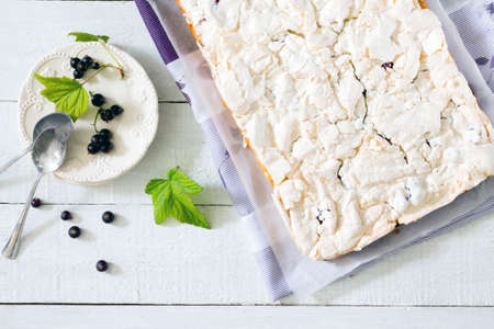 Homemade pie with meringue and black currant on a white wooden table, top viewの写真素材