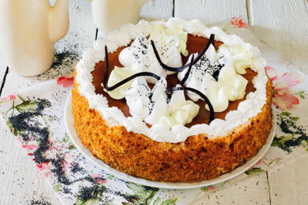 Honey cake with whipped cream and caramel on a white wooden background.