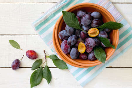 Plum in a ceramic bowl on a white wooden table, top view