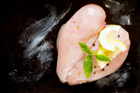 Raw Chicken fillet with lemon and basil on a dark backgroundの写真素材
