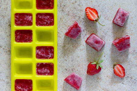 Ice made from strawberries for summer drinks with copy space on brown stone background.の写真素材