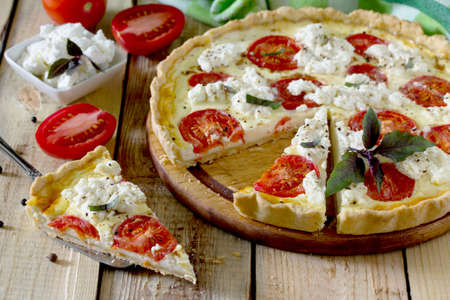 A classic quiche Lorraine pie with soft feta cheese and tomatoes in a baking dish on a table in a rustic style.の写真素材