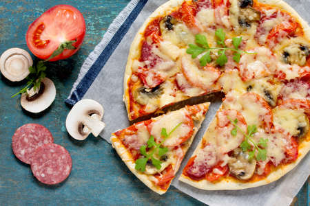 Tasty Italian pizza with pepperoni, tomatoes, cheese and mushrooms on a vintage wooden table.の写真素材