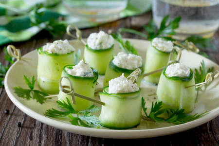 Cucumber rolls stuffed with feta cheese, dill and olives on a wooden table.の写真素材