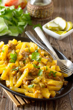 Potatoes with pickles, meat and tomato sauce, vegetable stew on a wooden table