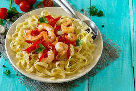 Italian pasta tagliatelle with shrimp and sweet peppers paprika, decorated with basil on the table in a rustic style. Copy space.の写真素材