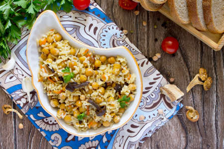 Vegetarian vegetable pilaf chickpea and wild mushrooms on a wooden table, a healthy diet, diet, vegetarian cuisine and the concept of cooking.の写真素材