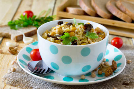 Vegetarian vegetable pilaf with chickpeas and wild mushrooms on a rustic background, healthy eating, diet, vegetarian cuisine and the concept of cooking.の写真素材
