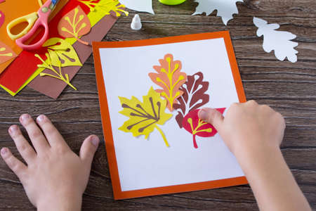 Autumn leaves of colored paper on a wooden background. Child glues the paper sheets. Sheets of paper...