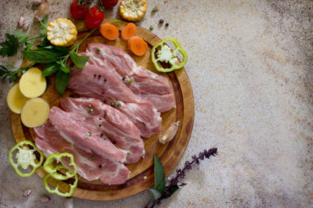 Fresh raw meat pork tenderloin with vegetables on a cutting board. Stone background. Copy space.の写真素材