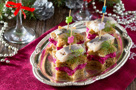 Holiday appetizer: Canapes in the form of a star with pickled herring, beetroot dip and dill on a festive Christmas table.の写真素材