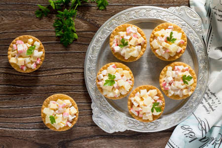 Holiday appetizer: tartlets with crab sticks, cheese and pineapple on a wooden table.の写真素材