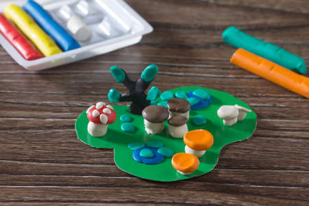 Child sculpts plasticine mushrooms tree and autumn leaves. Consumables for kids arts and crafts on a wooden table. Plasticine idea for children. Activities in the kindergarten and at home.の写真素材