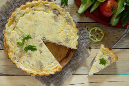 A classic quiche Lorraine pie with potatoes, meat and cheese in a baking dish on a table in a rustic...