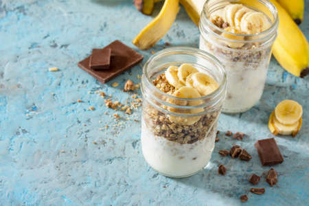Granola, healthy breakfast. Copy space. Granola with yogurt, chocolate and banana on blue concrete table.の写真素材