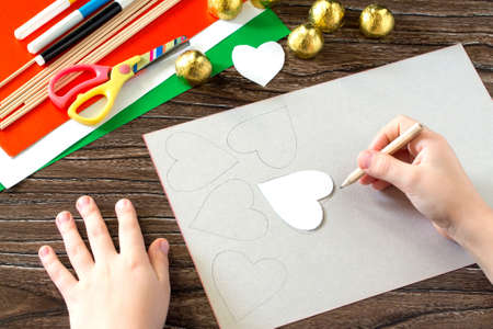 The child cuts out a pattern gift bouquet of flowers heart made of paper and candy on Valentine's Day. Children's art project, a craft for children. Hand-made.の写真素材