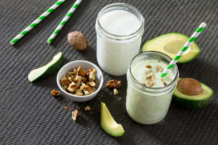 Healthy green cocktail with avocado and walnuts in a bank of glass on dark stone background. Yogurt...