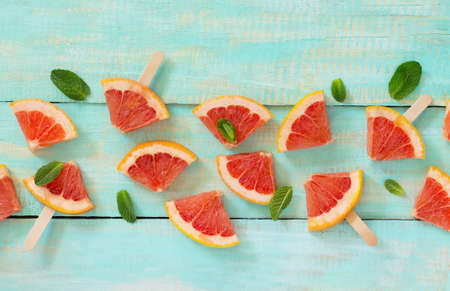 Slices of red grapefruit popsicle on a vintage wooden background, copy space. The concept of a healthy diet and detox diet.の写真素材