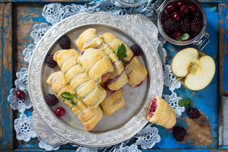 Homemade apple mini strudel with fresh apples, cherries, blackberries and sugar powder on a blue antique wooden background. Top view.の写真素材