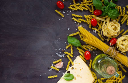 Ingredients for cooking Italian pasta - spaghetti, fusilli, fettuccine, basil, cherry tomato, garlic, pepper and cheese. Top view with space for text.の写真素材