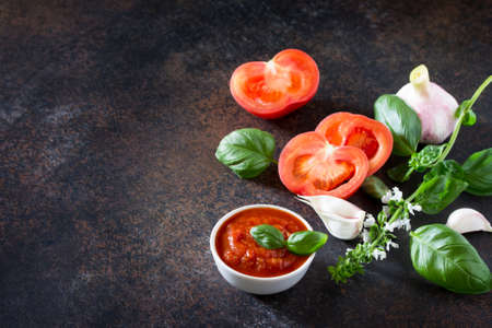 Tomato ketchup sauce in a bowl with spices, basil leaves and tomatoes on the kitchen table. Copy space.の写真素材