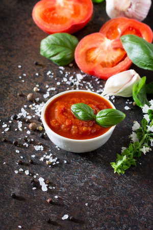 Tomato ketchup sauce in a bowl with spices, basil leaves and tomatoes on the kitchen table. Copy space.の写真素材