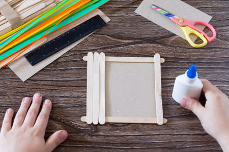 The child glues the details to a gift photo frame made of wooden sticks. Handmade. Project of...