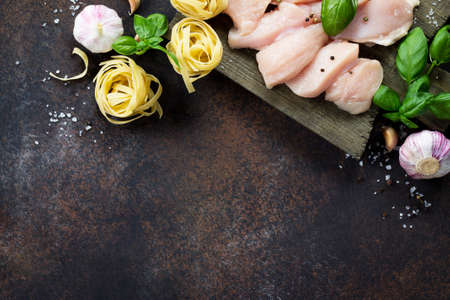 Fresh meat. Preparation of Italian cuisine pasta with chicken fillet and various spices on dark concrete, stone or slate. Food background.の写真素材
