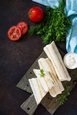 Shaurma lavash with fried chicken meat, fresh vegetables and creamy sauce on a background of brown...