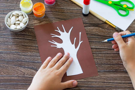 The child draws details of the application. Postcard autumn tree with multi-colored leaves of pumpkin leaves. Children's art project, craft for children. Craft for kids.の写真素材